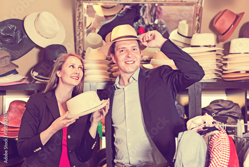 Girl and male try on modern hats at the boutique