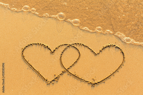 Two hearts drawn in the sea sand with the soft wave.