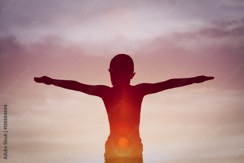 Silhouette of happy little boy at sunset sky