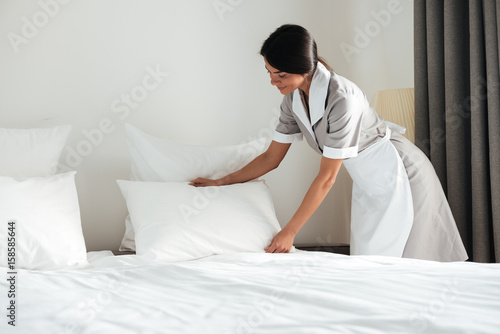 Tableau sur toile Young hotel maid setting up pillow on bed
