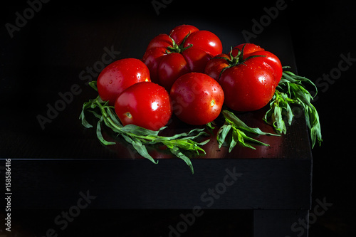 Juicy tomatoes with estragon and water dropletson a wooden dark background photo