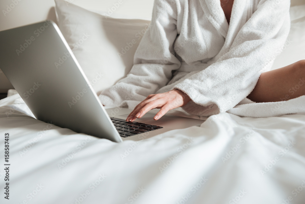 Naklejka premium Cropped image of a woman in bathrobe on bed and using laptop