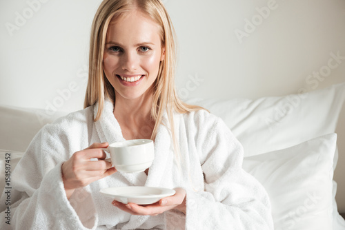 Happy smiling woman in bathrobe holding cup of coffee