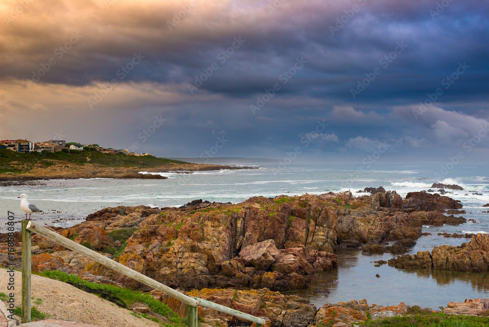 Rocky coast line on the ocean at De Kelders, South Africa, famous for whale watching. Winter season, cloudy and dramatic sky.