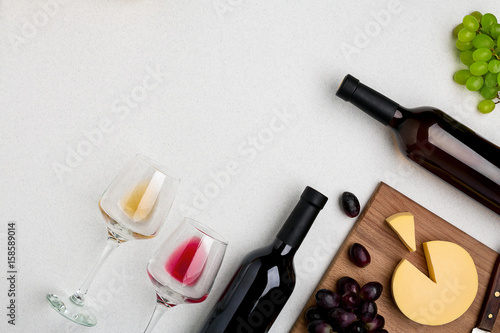 Two wine glasses with red and white wine,bottles of red wine and white wine, cheese on white background. Horizontal view from the top.