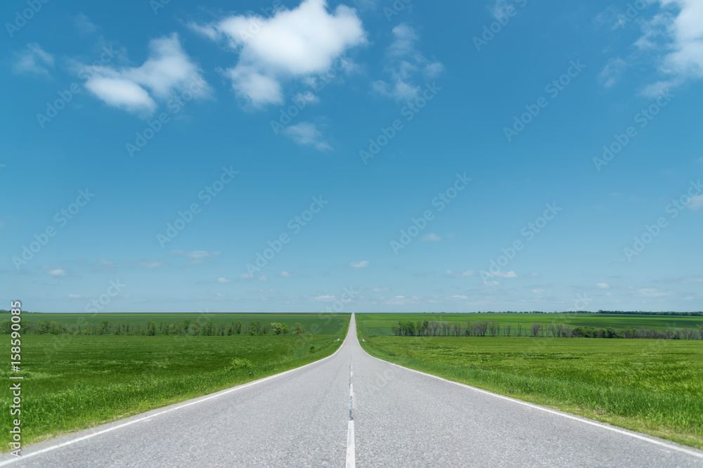 A wide asphalt road between green fields
