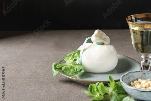 Italian fresh burrata cheese in a ceramic mash with green salad and olive oil. Dark background.