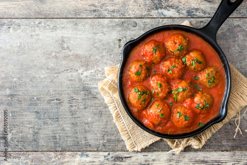 Meatballs with tomato sauce in iron frying pan on wooden table. Top view photo