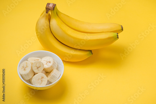 A banch of bananas and a sliced banana in a dish over yellow background.