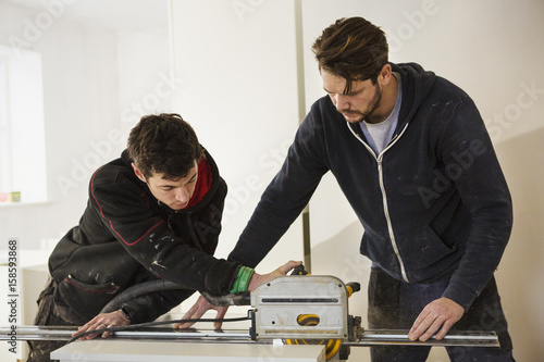 Two builders, cutting plasterboard with a circular saw.