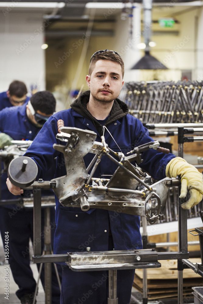 Male skilled factory worker in overalls wearing one protective glove, working on a bicycle frame in a factory.