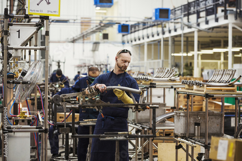 A man wearing one protective glove with sunglasses on his head,  skilled factory worker working on bicycle parts in a factory. photo