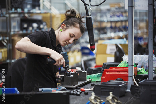A young woman using a power tool, a skilled factory worker assembling cycle parts. photo