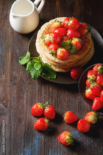 Stack of homemade Pancakes with fresh Wild Strawberries on a plate on a wooden background.