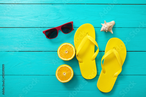 Yellow flip flops, red sunglasses, shell and orange fruit on blue wooden background. Top view and summer time.