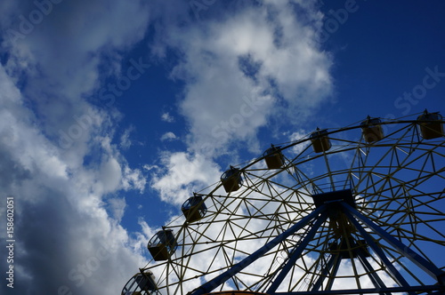 Attraction Ferris wheel on a background of bright summer blue sky with white clouds