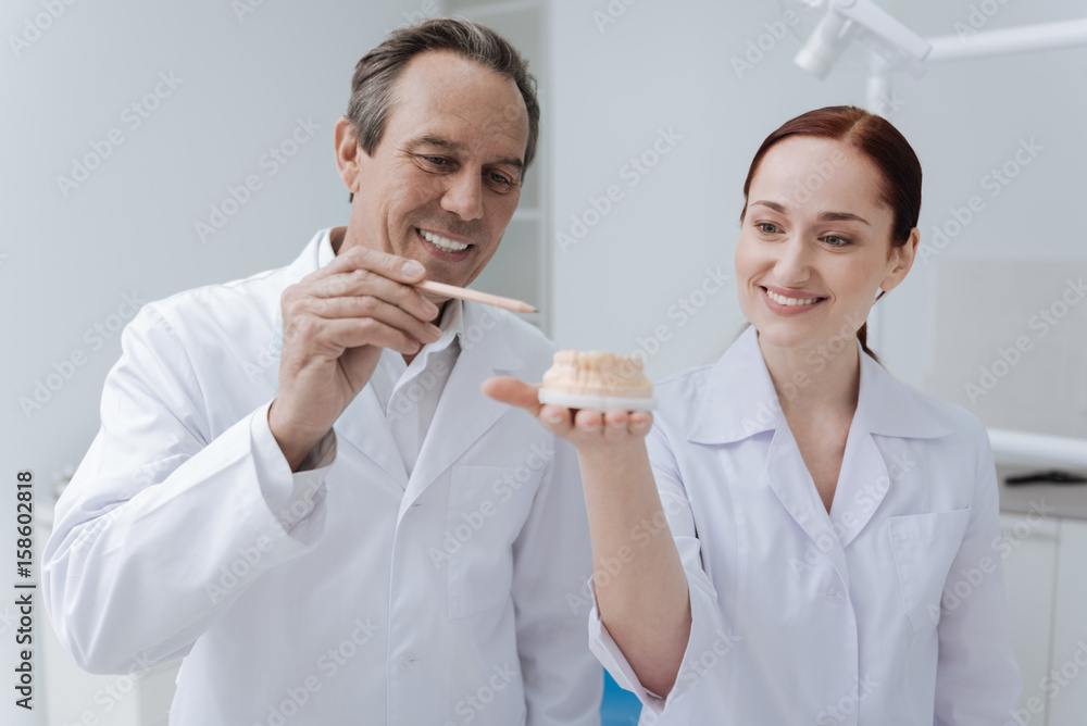 Positive delighted stomatologist teaching new intern Positive delighted stomatologist teaching new intern