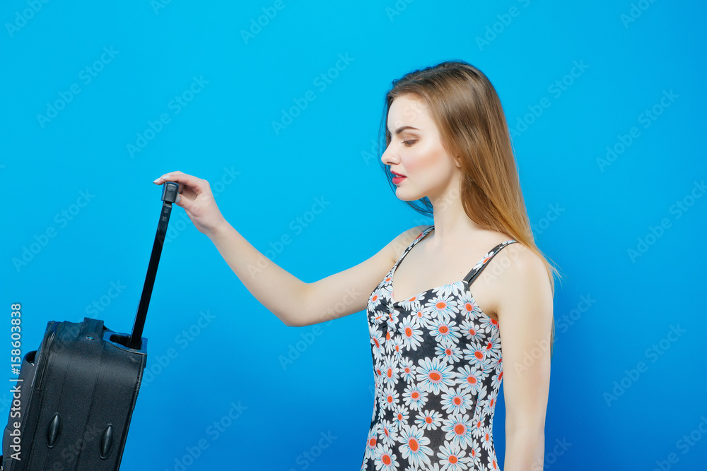 Pretty Woman with Dark Long Hair is Holding Travel Bag on Blue Background in Studio. Vacation Concept. Pretty Woman with Dark Long Hair is Holding Travel Bag on Blue Background in Studio. Vacation Concept.