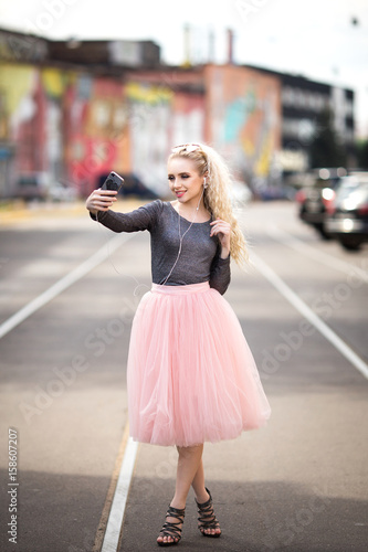 Young smiling cheerful blonde girl making selfie while standing on the street © Anastasiya 