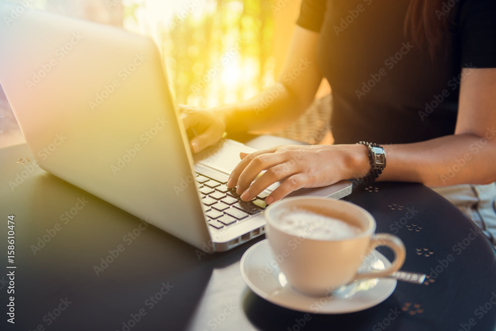 Young woman sitting at desk and typing on laptop to working online at computer in the morning. Concept of networking and occupation, hands close up. Female working on an outdoor cafe.