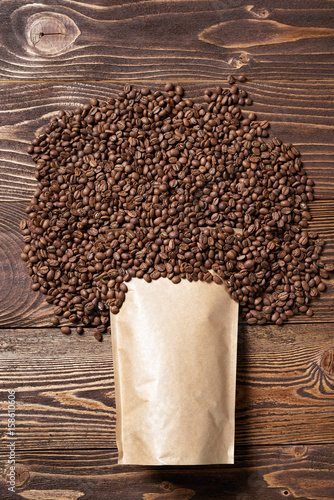 Mock-up craft paper pouch bag top view over wooden background with coffee beans over