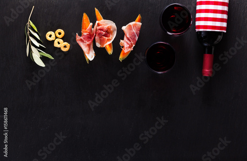 Classic Italian appetizer of prosciutto and melon with red wine and taralli on a dark stone naturanom