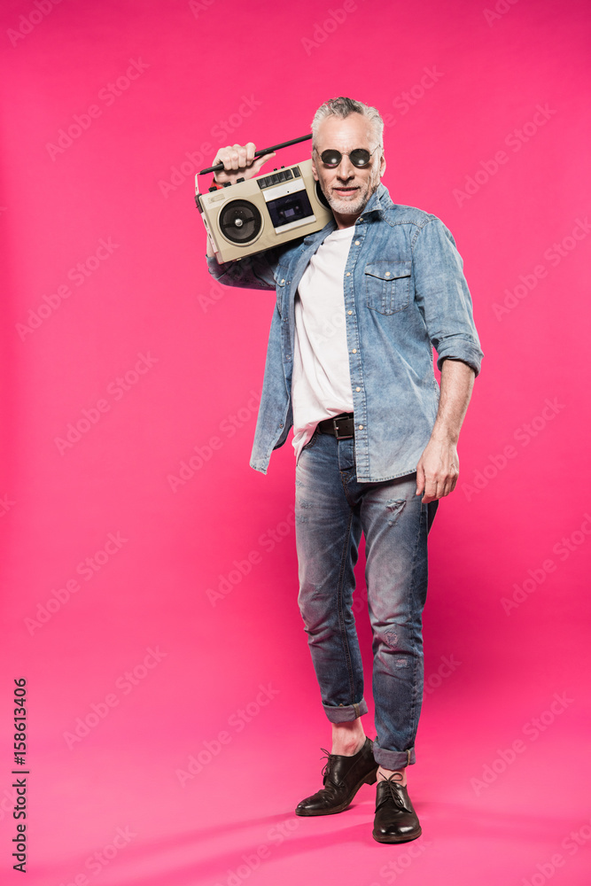 senior stylish man holding tape recorder on shoulder and looking at camera isolated on pink senior stylish man holding tape recorder on shoulder and looking at camera isolated on pink