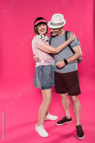 stylish cheerful man and woman hugging each other isolated on pink