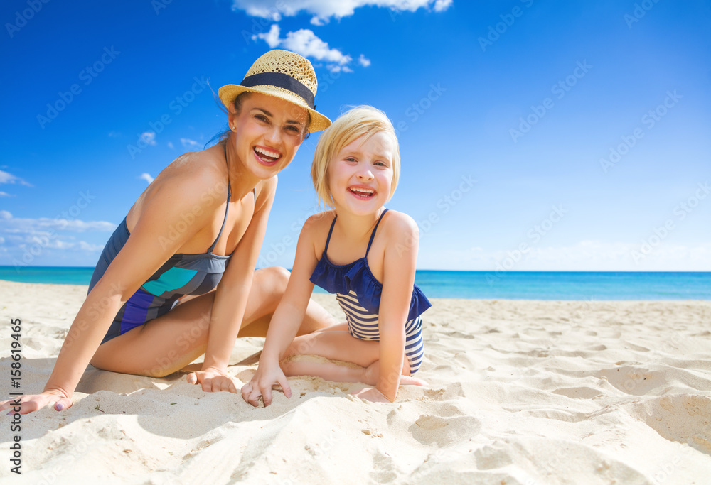 smiling young mother and daughter in swimwear on seacoast
