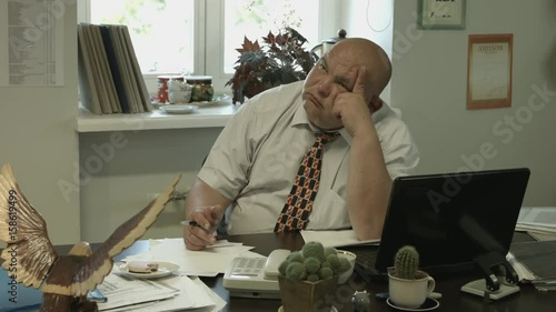 Ungraded: A bored fat bald office worker reluctantly pays attention to the visitor outside the frame, turns and looks straight to the camera.