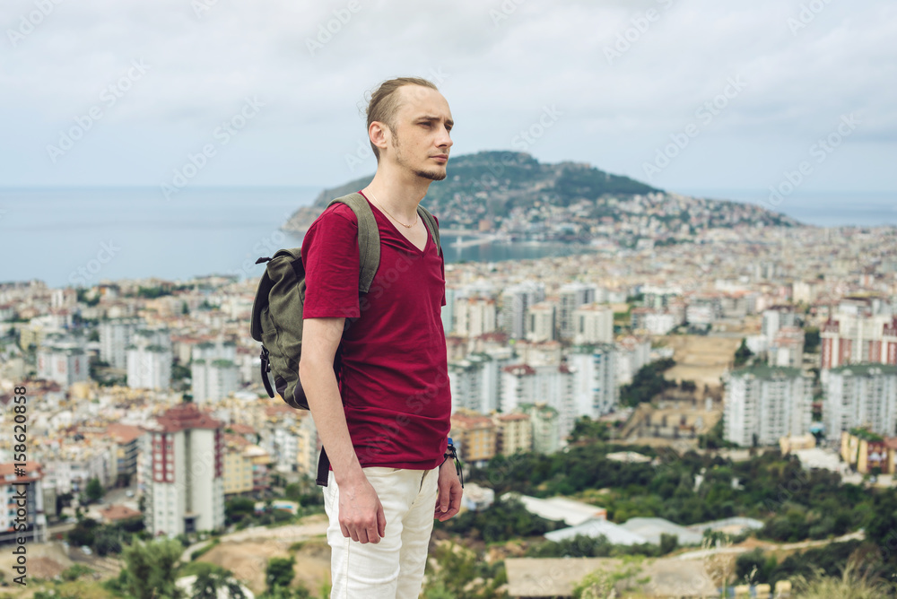 Man traveler with backpack explores the city looking at the panoramic view of the city and the coast. Man traveler with backpack explores the city looking at the panoramic view of the city and the coast.