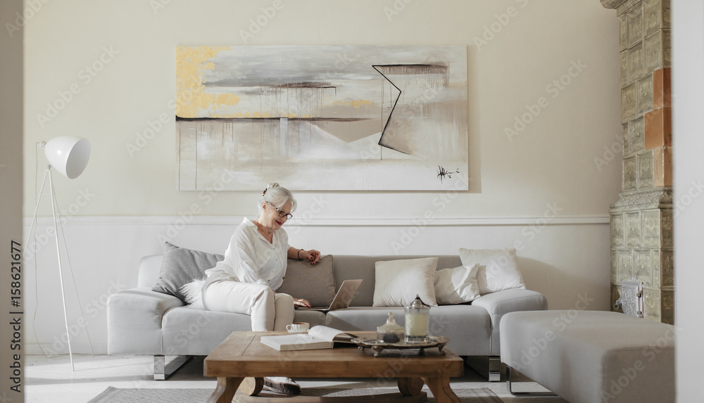 Pretty senior Caucasian woman sitting at home and reading on her laptop. Pretty senior Caucasian woman sitting at home and reading on her laptop.