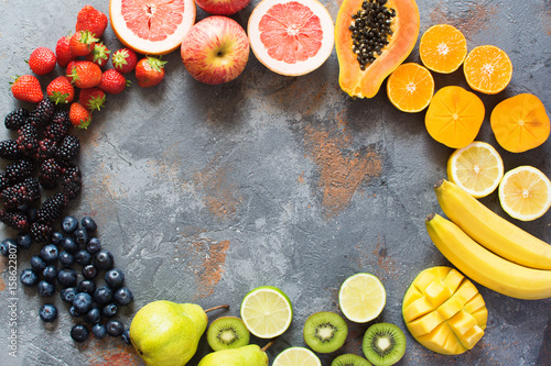 Rainbow color fruits arranged in a circle  strawberries  blueberries  mango  orange  grapefruit  banana  apple  grapes  kiwis  papaya on the grey background  copy space for text  selective focus