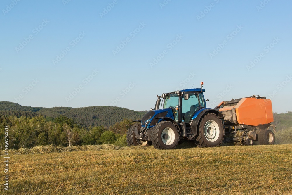 Blue tractor on the pasture.. Agricultural work on the farm in the Czech Republic. Blue tractor on the pasture.. Agricultural work on the farm in the Czech Republic.