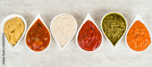 Top view on a set of sauces on a light gray stone background.