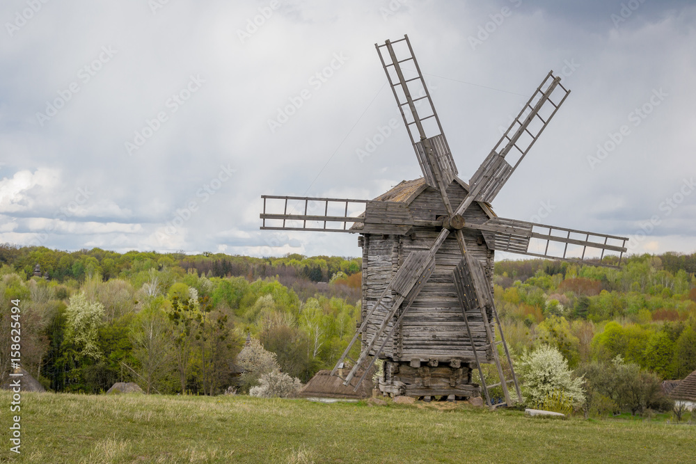 National Museum Pirogovo in the outdoors near Kiev. Ancient traditional wooden windmill, beautiful spring landscape with sky. National architecture.