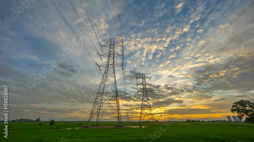 Time lapse 4k Footage of Sunrise With Two Transmission Power Line Tower on paddy field as a Foreground. Showing moving and changing colour clouds as the sun setting.