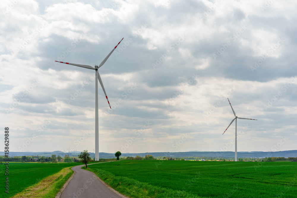 Road between green fields leading to two wind turbines Road between green fields leading to two wind turbines