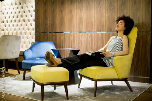 Young woman sittinh on a yellow chair and reading a book