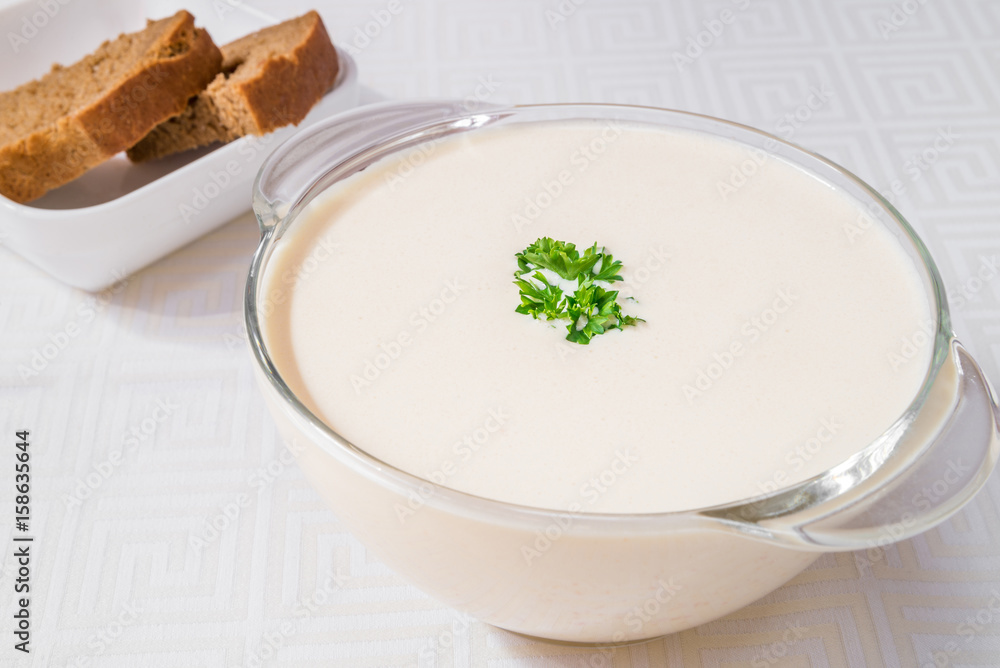 Tasty breakfast. White soup in a transparent plate, bread in the background. Horizontal frame