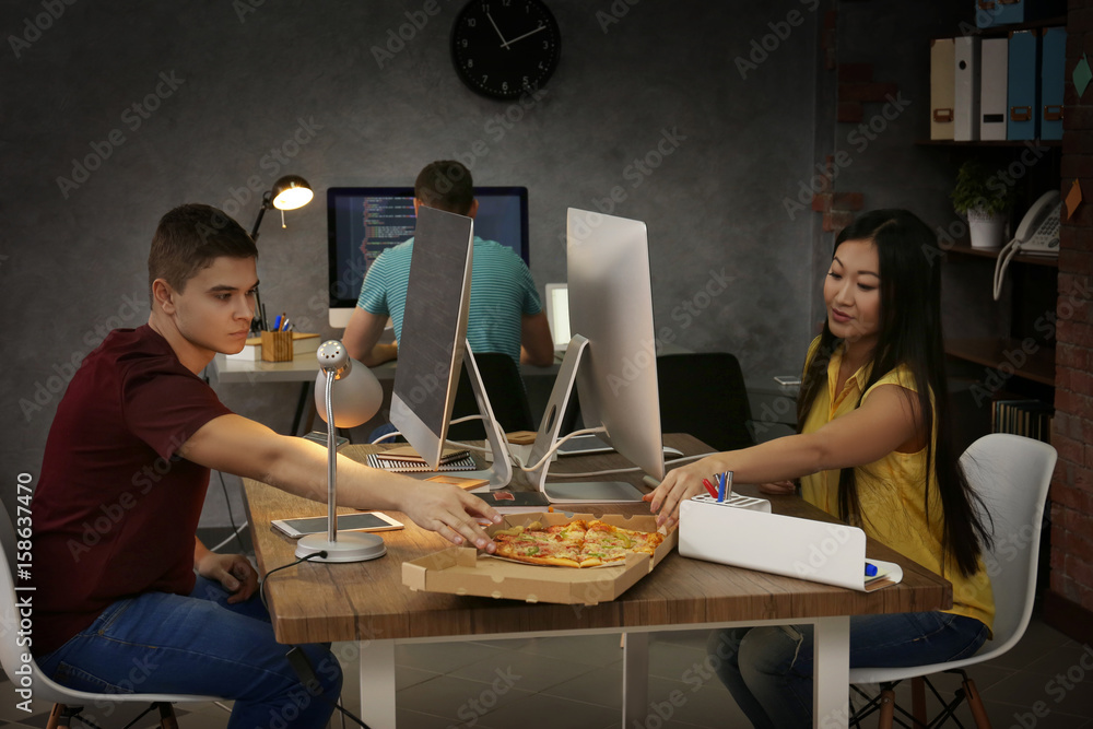 Young programmers eating pizza while working in office Stock Photo ...