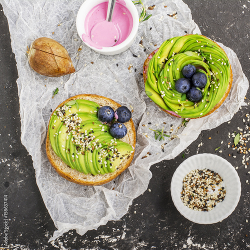 Round buns for breakfast with avocado in the form of a rose with a sauce of yogurt with a variety of sesame seedsAgainst a dark background . Top view. The concept of healthy nutrition
