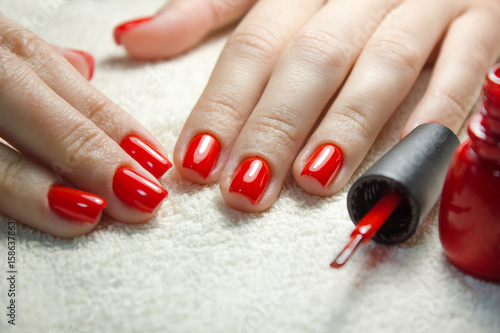 Beautiful manicured woman's nails with red nail polish on soft white towel.