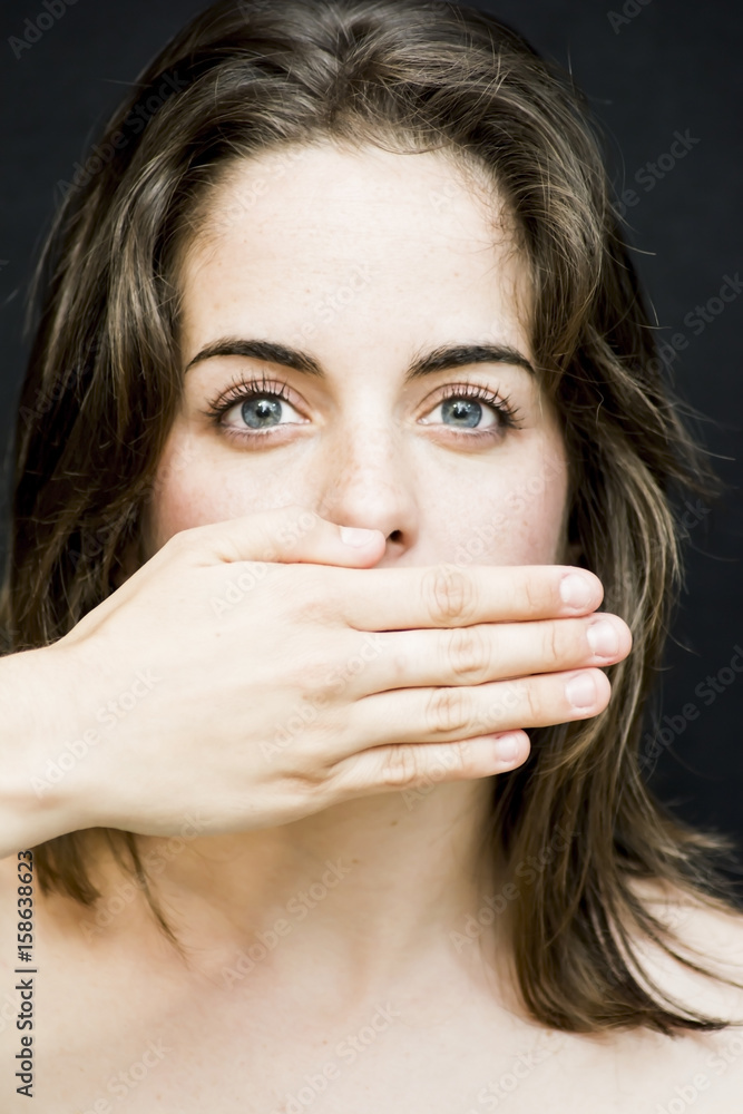 Portrait of a beautiful woman covering her mouth with her hand on black background Portrait of a beautiful woman covering her mouth with her hand on black background