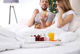 Tray with breakfast on bed and happy couple