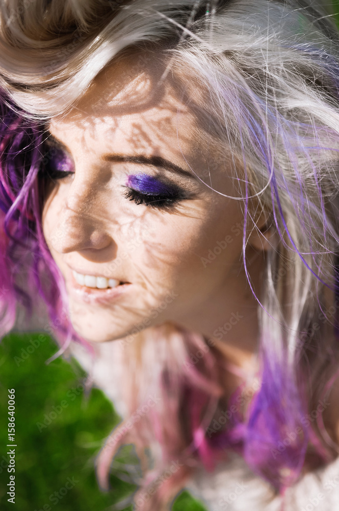 Naklejka premium close-up portrait of a beautiful sexy young blonde girl hipster with lilac and pink hair on the background of blooming lilacs, posing