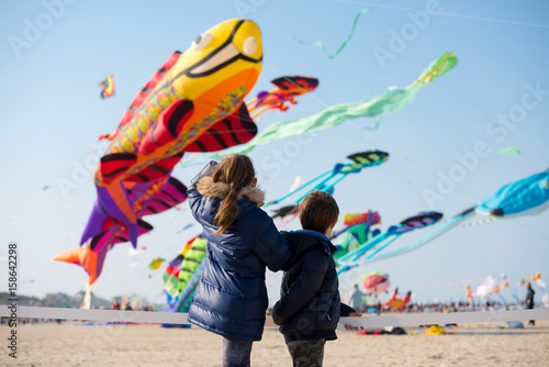 Children looking at group of colorful large kites flying in clear sky 
