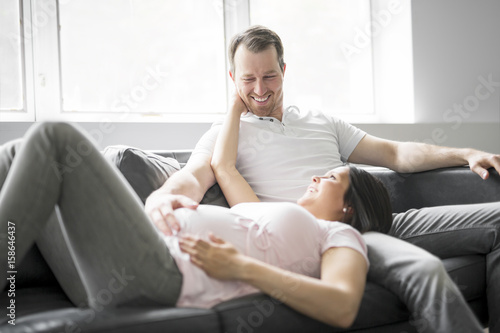 Couple With Pregnant Woman Relaxing On Sofa Together