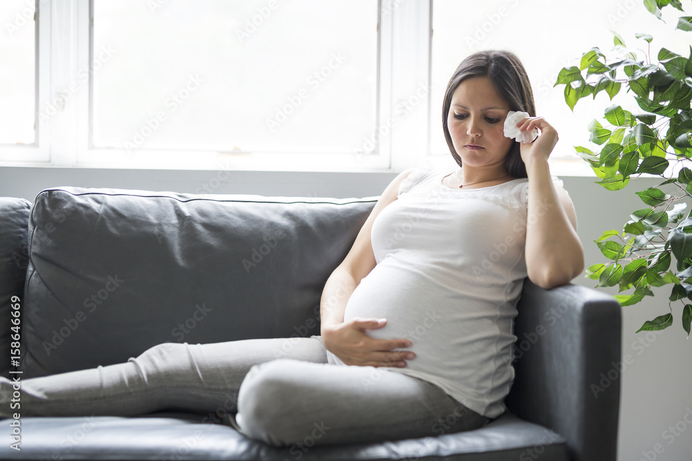Obraz premium Sad pregnant woman lying on sofa at home