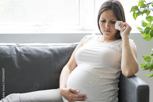 Sad pregnant woman lying on sofa at home